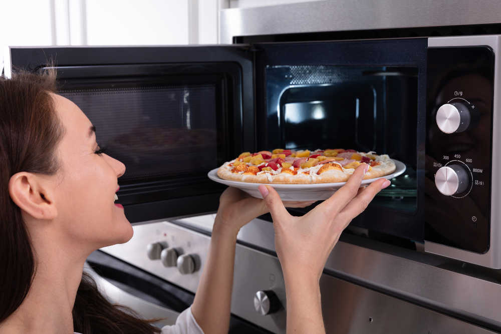 Kobieta wyjmująca pizzę z kuchenki mikrofalowej